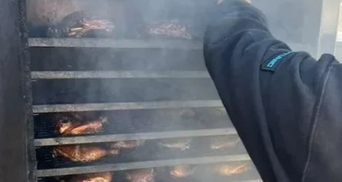 A dad checking racks of meat in a large outdoor smoker